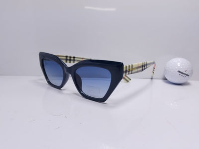 Black cat-eye sunglasses with blue lenses next to a golf ball on a white surface