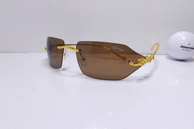 Gold-framed sunglasses with brown lenses on a white surface next to a golf ball.