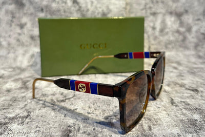 Sunglasses with decorative frames on a textured surface, Gucci box in the background