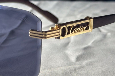 Cartier sunglasses with gold frame and black arm on a light gray background