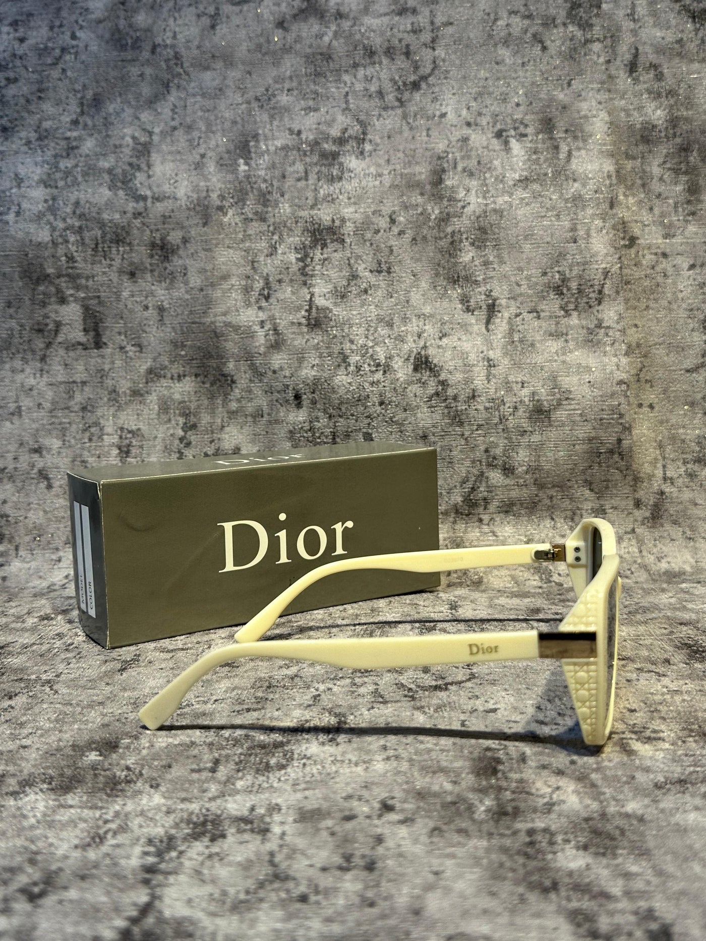 Gold Dior sunglasses on a textured surface with a Dior box in the background.