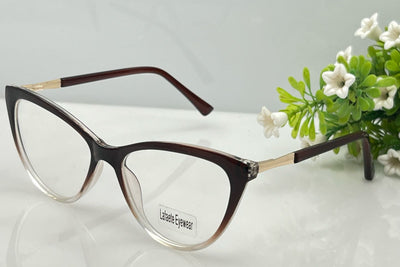 Eyeglasses with brown frame and gold accents on a light gray background with greenery.